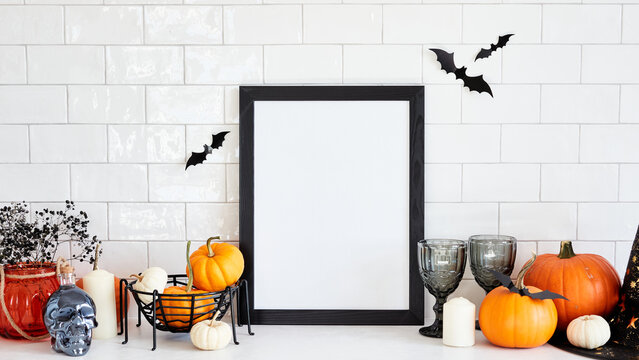 Halloween holiday concept. Scandinavian living room interior with picture frame mockup, Halloween home decor, pumpkins on white desk table. Halloween poster template.