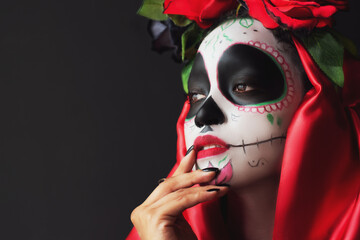 beautiful latin woman with mexican sugar skull makeup, between shadows and flowers decoration