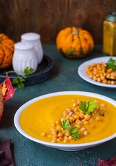 Creamy pumpkin soup with fried chickpeas garnish in a white ceramic plate on a green concrete background. Thanksgiving Day