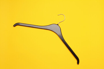 Minimalist top view flat lay empty black plastic clothes hanger at yellow background. Sale store design, shopping concept.  
