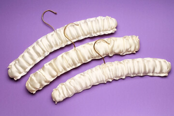 Top view flat lay different empty silk clothes hangers at violet purple background. Sale store design, shopping concept.  