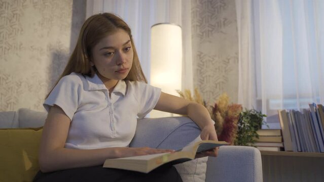 Young woman reading a book.
Young girl reading a book at home, focused on the book.
