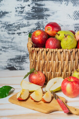 Basket with a harvest of fresh pears and apples on a white table. Sliced pears and apples on a cutting board. Space for text