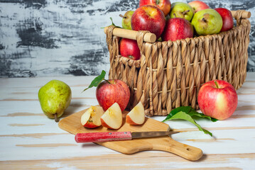 Sliced apples on a cutting board. Basket with a harvest of fresh pears and apples on a white table.