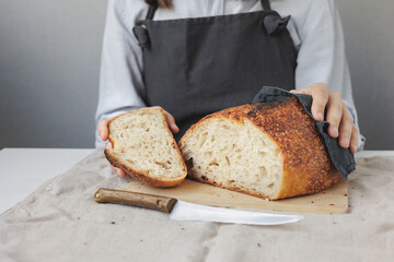 baker woman in a dark apron is cooking bread in the kitchen, a cook in a pastry shop is holding bread in her hands. fresh bread is on the cutting board. Baking and confectionery in a bakery or