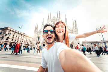 Happy couple taking selfie in front of Duomo cathedral in Milan, Lombardia - Two tourists having...