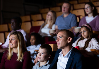 Family spending time together in cinema. Selective focus of young father hugging his preteen son while watching movie