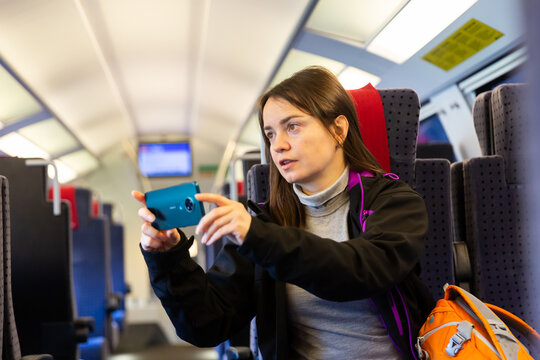 Woman using her smartphone to photograph view from train window.