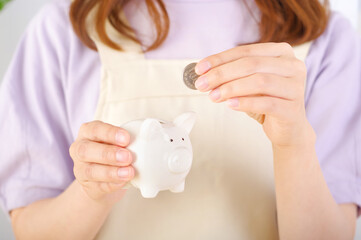 豚の貯金箱にお金を入れるエプロン姿の女性
