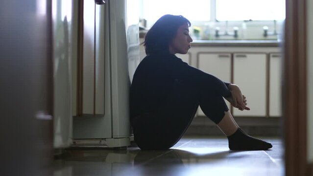 Woman suffering from depression sitting on floor at home having emotional angst and pain. Sad unhappy person suffering from mental illness