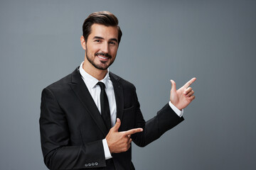 Business man has his hands up pointing his finger and smiling with his teeth open mouth in a business suit on a gray background portrait