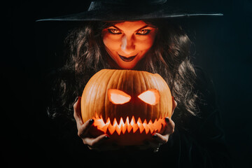 Mysterious black witch with pumpkin as head of jack-o-lantern on dark backdrop. Scary symbol of...