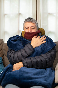 Homme malade qui a froid. il porte une &eacute;charpe, un gros manteau d'hiver dans sa maison et il grelotte