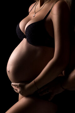 Pregnant belly. Pregnant girl on a black background. Belly of a pregnant girl in underwear. The husband touches the pregnant wife's stomach. Studio shooting. Vertical photo. Woman holding her belly.