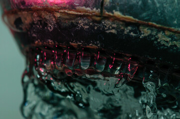 Closeup of water flowing from a rusty faucet, backlit with pink and green, at short exposure, water texture