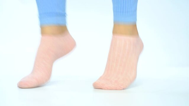 Female legs in pink socks jumping on white background close-up.