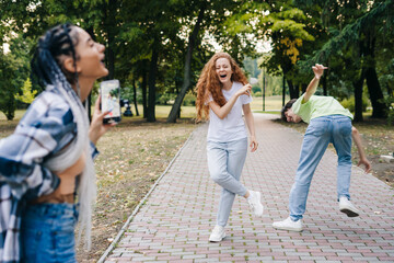 Young caucasian woman shooting her friends dancing in the park for making video for social media,...