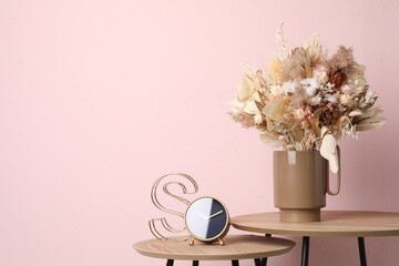 Stylish ceramic vase with dry flowers and leaves on wooden table near pink wall. Space for text