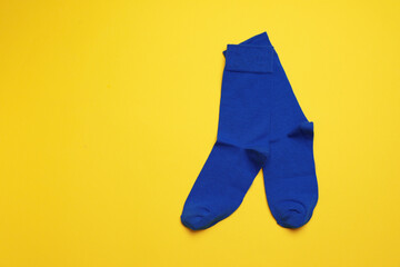 Blue socks on yellow background, flat lay. Space for text