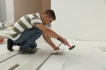 Professional worker using hammer during installation of new laminate flooring indoors