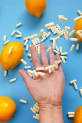 White capsules of vitamin C in a hand and yellow lemon citrus fruits.Vitamin C.Taking vitamin C tablets. Tablets fly into the hand.Health and medicine 