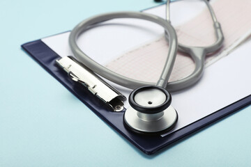 Clipboard with stethoscope and cardiogram on turquoise background, closeup