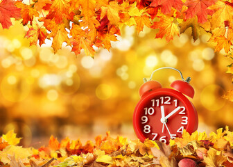 Alarm clock on table and beautiful autumn leaves against blurred background, space for text. Time change concept