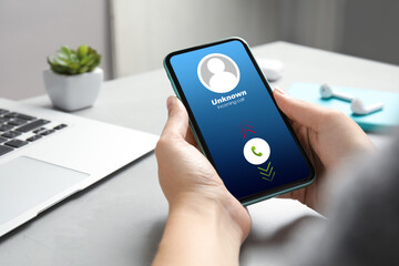 Woman holding smartphone with incoming call from unknown caller at table, closeup. Be careful -...