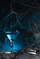 Halloween martini alcoholic cocktail on scary dark blue background with smoke, twisted branches,...