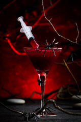 Halloween alcoholic cocktail bloody martini with syringe on scary dark red background with twisted...