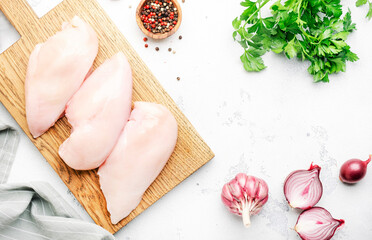 Raw chicken breast fillet, meat on cutting board prepared for cooking with garlic, thyme, spices and pepper. White kitchen table, top view