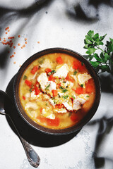 Warming autumn soup with red lentils, chicken fillet, vegetables, spices and paprika, comfort food. White table, hard light with leaf shadows, top view