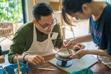 Focus couple potter working on potters wheel making ceramic pot from clay in pottery workshop. Couple in love working together in potter studio workshop.