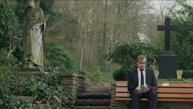 sad man sitting on bench in cemetery, medium shot