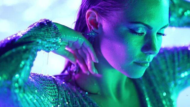 Pretty wet woman in pool water under neon glowing color light. Party, attractive girl in shining dress dancing slowly, night time. Work as model, influencer
