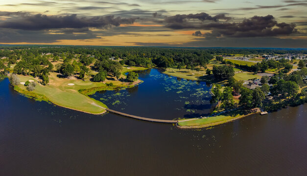 an aerial panoramic shot of a blue waters of Houston Lake surrounded by a golf course and lush green trees, grass and plants with powerful clouds at sunset in Perry Georgia USA