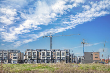 Fototapeta na wymiar View of new home construction in a field, blocks of townhouses, cranes, blue sky sunny, grass field foreground, nobody