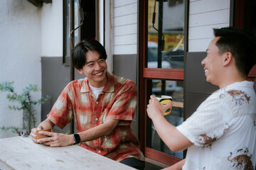 カフェのテラスで飲み物を片手に談笑する二人のゲイの男性