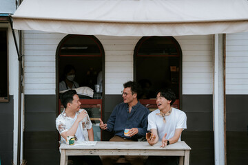 カフェのテラスでテーブルを囲み談笑する三人の男性