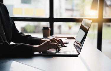 Close-up businessperson typing and searching data internet on laptop and hands holding pen at...