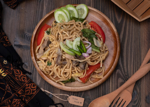 Mie Goreng Jawa or bakmi jawa or java noodle with spoon and fork. Indonesian traditional street food noodles from central java or Yogyakarta, Indonesia on wood background. Selective Focus. Close Up