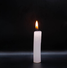 Vela de cera color blanco encendida con una llama en un fondo negro estilo mistico o espiritual