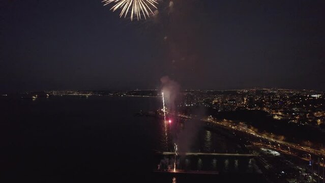 imagen aérea desde un dron de show pirotécnico. fuegos artificiales en el mar con explosiones y colores. Show lanzado desde muelle de pescadores. Se ve la ciudad iluminada de fondo
