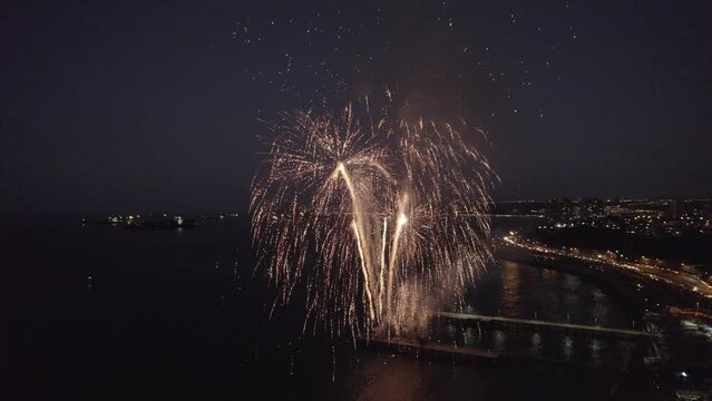 imagen a&eacute;rea desde un dron de show pirot&eacute;cnico. fuegos artificiales en el mar con explosiones y colores. Show lanzado desde muelle de pescadores. Se ve la ciudad iluminada de fondo