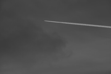 Airplane contrail against gray cloudy sky background with copyspace