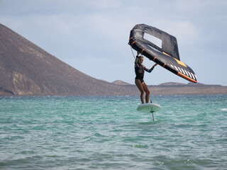 Caucasian young woman practicing water sport in the ocean wingfoil on hydrofoil surfboard