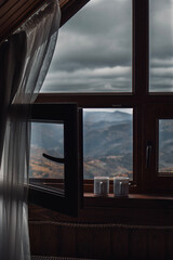 Two cups of tea on windowsill with opened window in front of mountains view