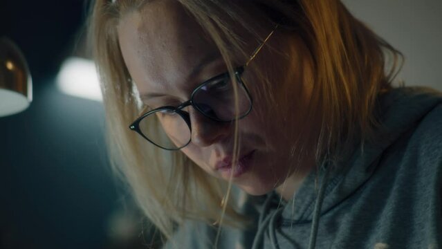 Closeup of the face of a young woman drawing a sketch by looking at the screen. Details of her face wearing black framed glasses and dressed in a grey hoodie.