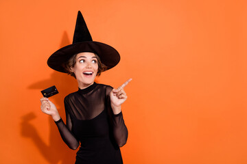 Photo of cheerful excited girl hold debit card look indicate finger empty space isolated on orange color background