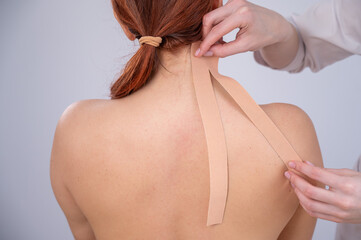 Female doctor glues kinesio tapes on the patient's shoulder. 